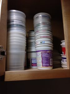 a kitchen cabinet full of empty and stacked plastic containers and large yogurt containers