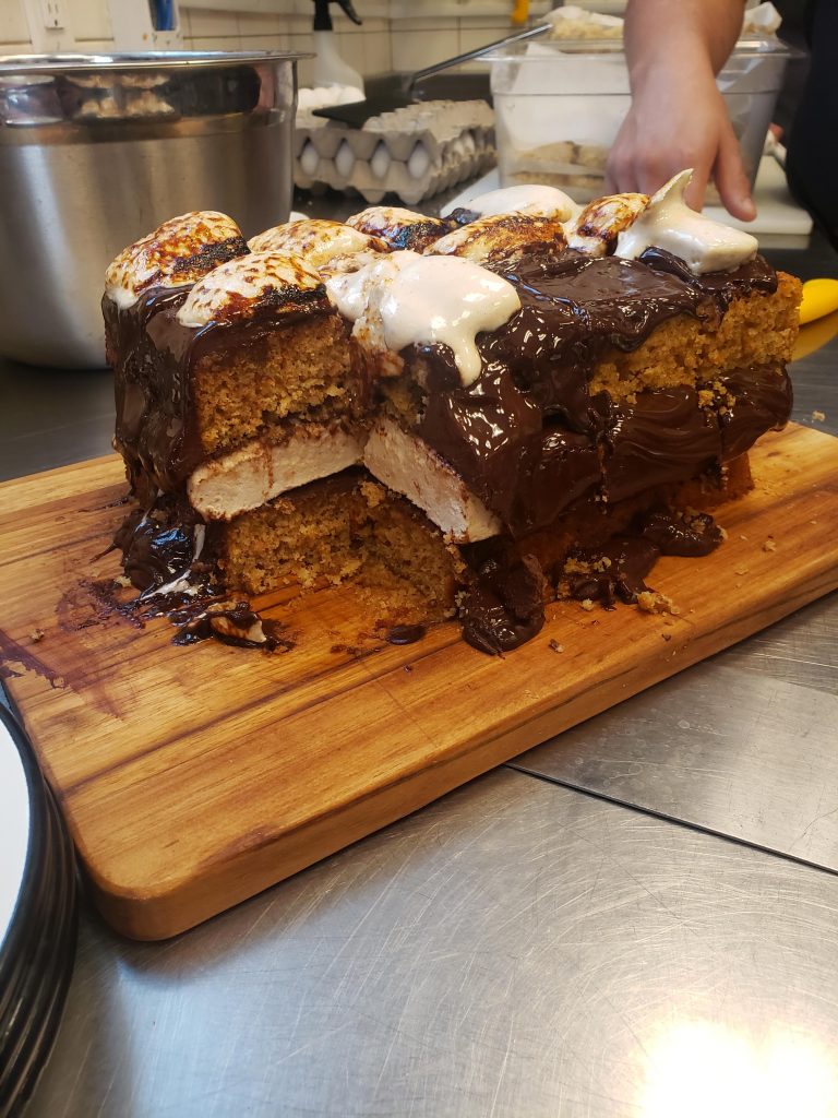a cake with a slice cut out of it, with a chocolate glaze and marshmallow on top