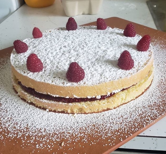 a cake on a wood board with powdered sugar sprinkled on it and raspberries arranged around the perimeter