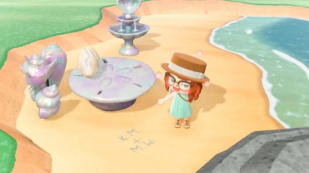 a player in animal crossing on a beach pointing at her initials and her wife's initials in the sand