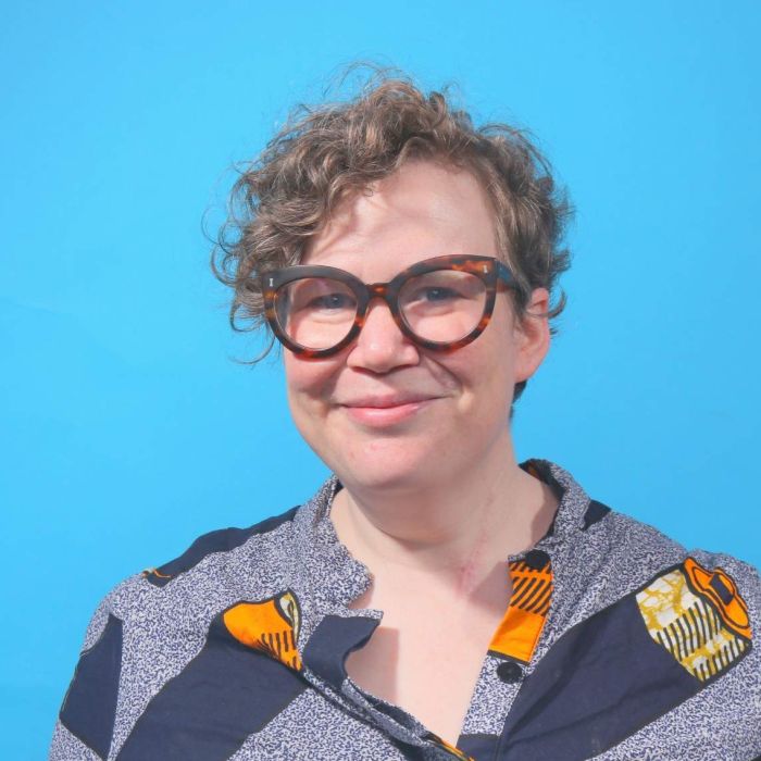 A woman wearing glasses in front of a blue background