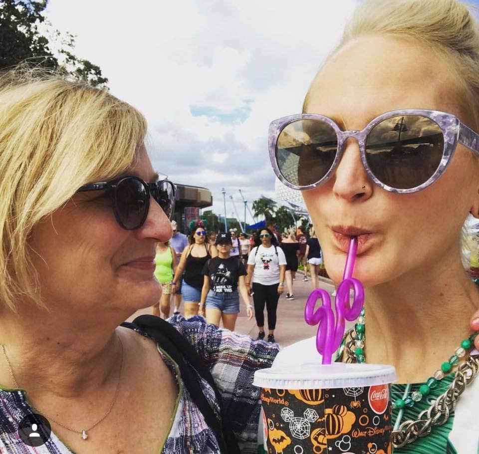 close up selfie of two women at Disneyland. They are wearing sunglasses and the woman on the right is drinking a beverage out of a Mickey Mouse fun straw