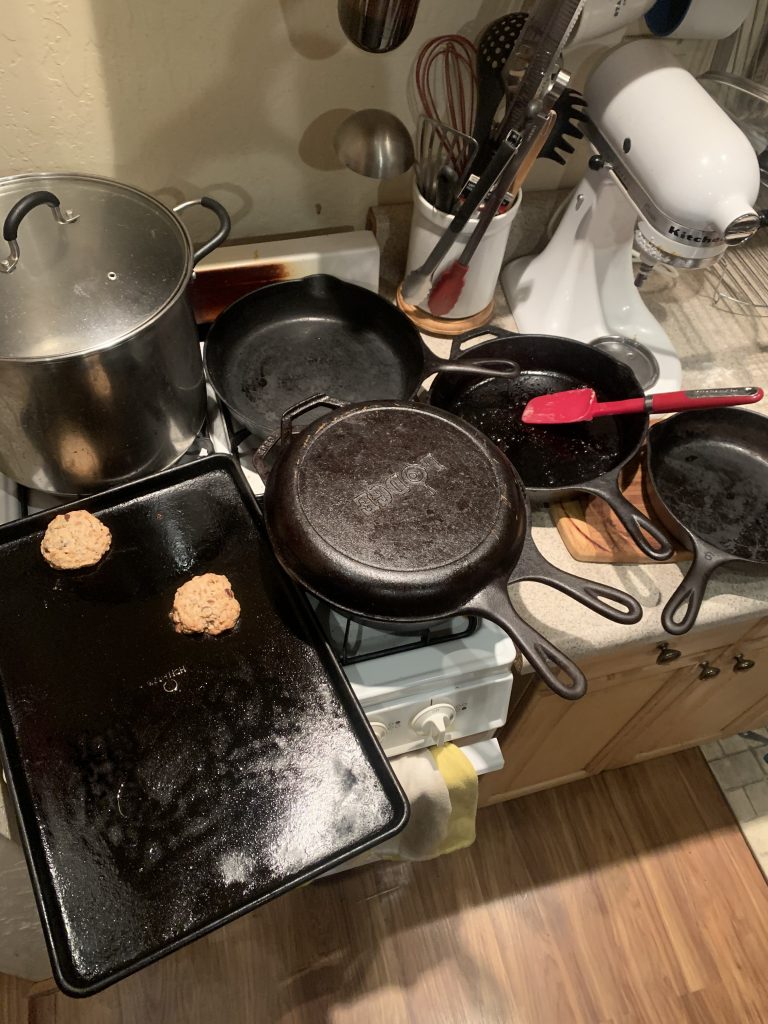 a stove and countertop full with with a stock pot, baking sheet, and 5 cast iron pans