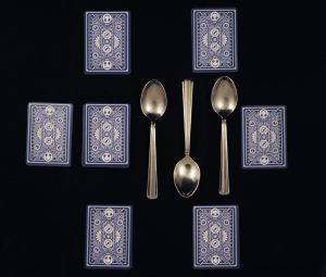 Maximum Fun playing cards and metal spoons arranged in the layout described in the rules for Spoons