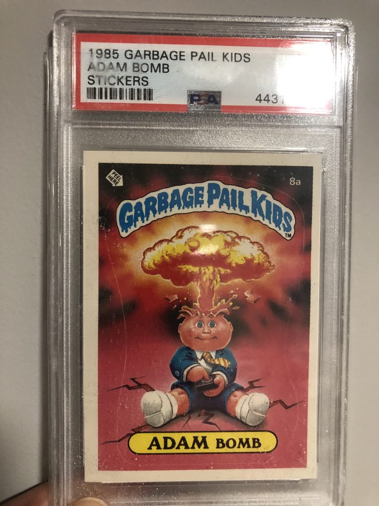 A Garbage Pail Kids trading card in a plastic collector case. There is a title and barcode label above the card that says, 