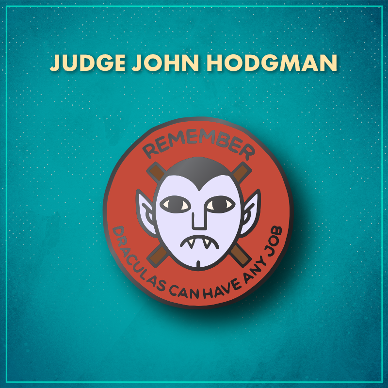 Judge John Hodgman. A red circle with the pale face of a frowning vampire with a widow’s peak and pointy ears in the middle. Behind the vampire are two crossed brown sticks, and the word "Remember" arches along the top of the pin, with "Draculas can have any job" arching along the bottom of the pin.