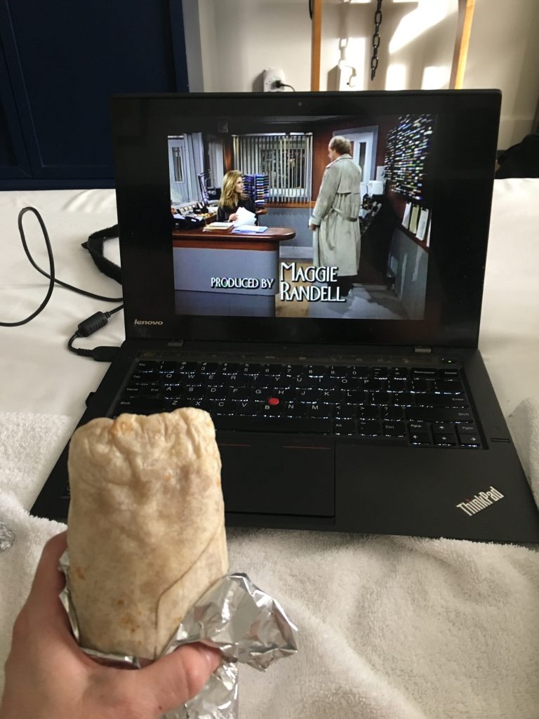 In the foreground is a hand holding a tightly wrapped burrito, in front of a laptop playing an episode of Frasier