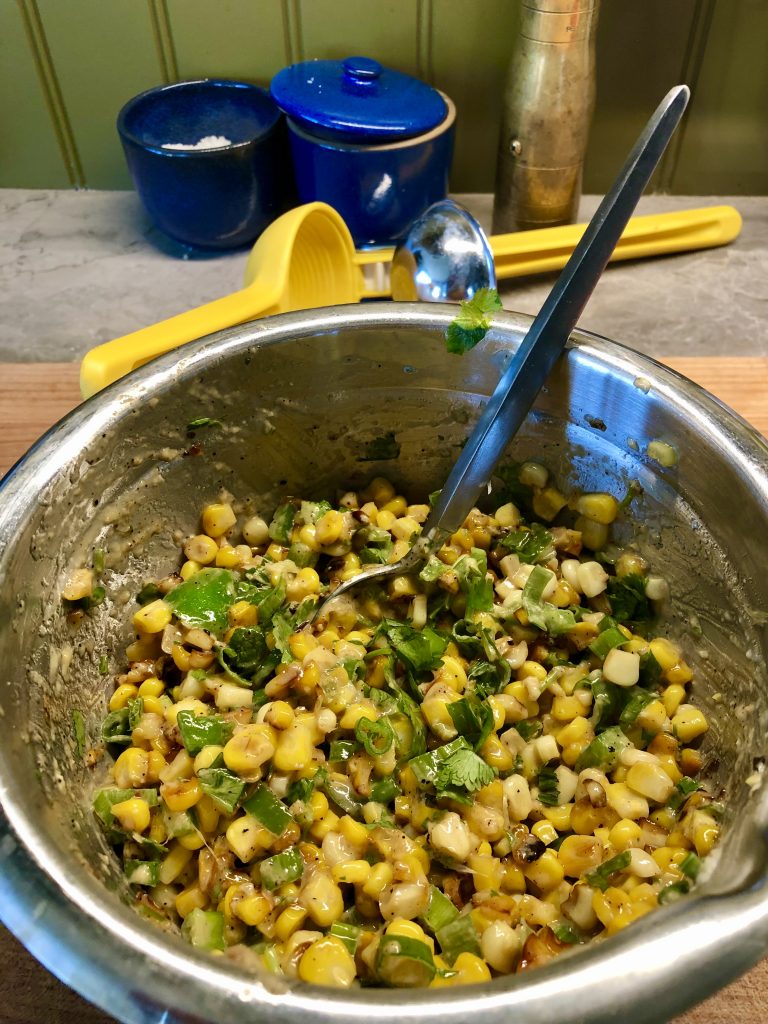 A metal bowl of homemade esquites: corn kernels, mayo, cilantro, and other ingredients.