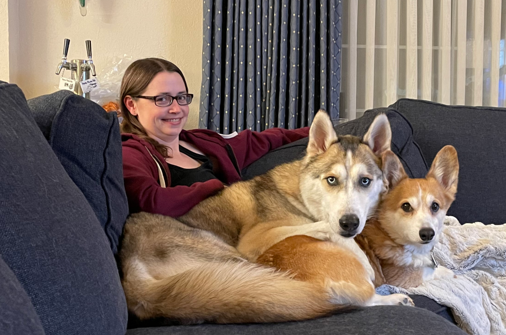 A woman sitting on a sofa with a husky and corgi in her lap
