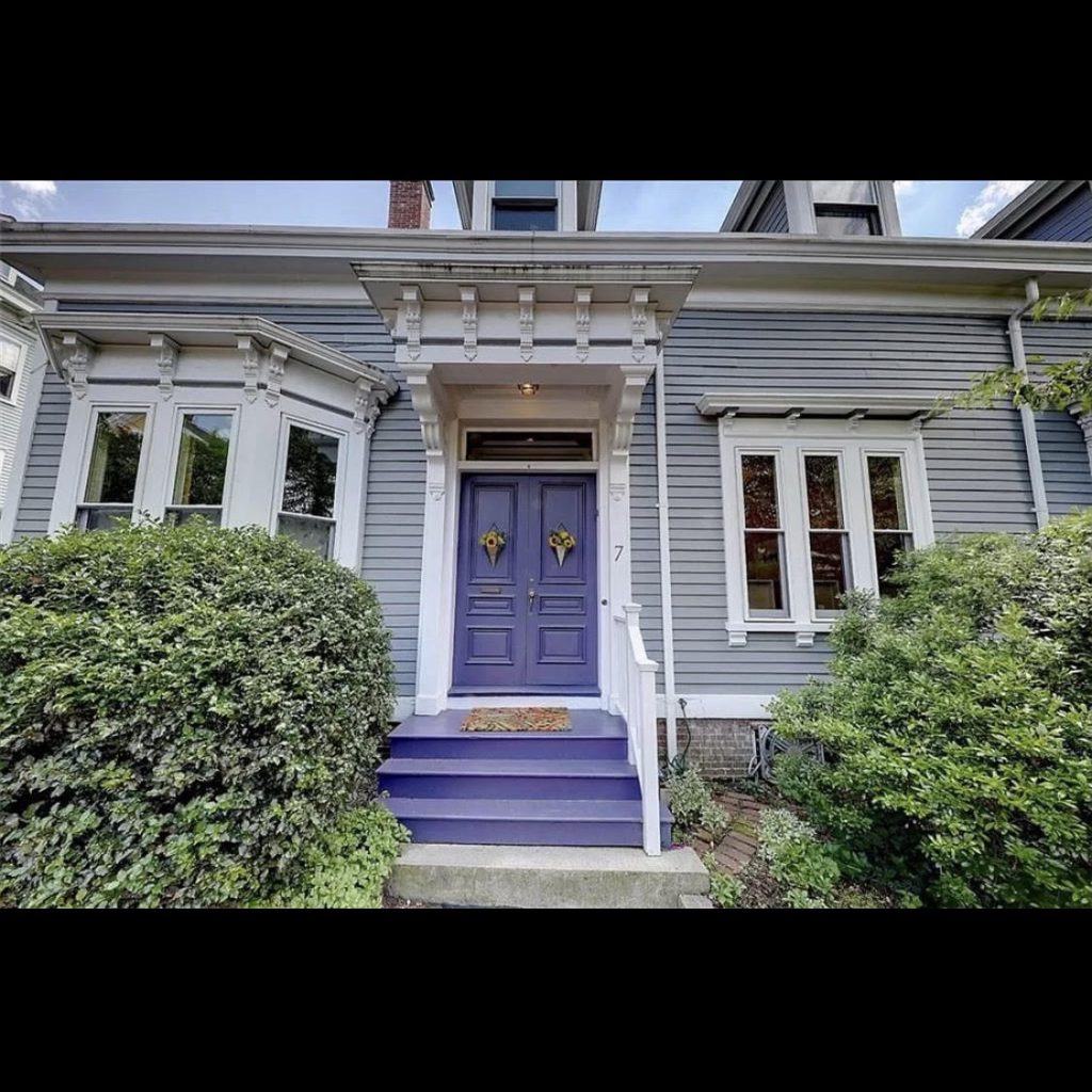 a gray New England home with a purple front door and purple front steps