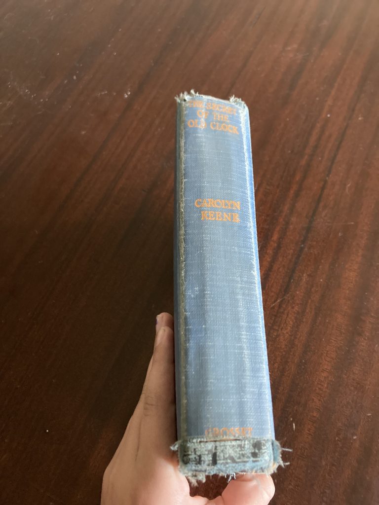 The spine of an old, hardcover book. The cover is blue fabric and the spine says 