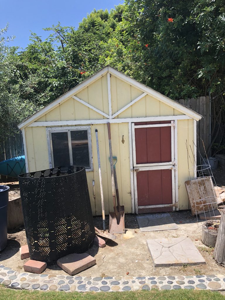 A kids' playhouse turned shed that is light yellow with white trim and a red door