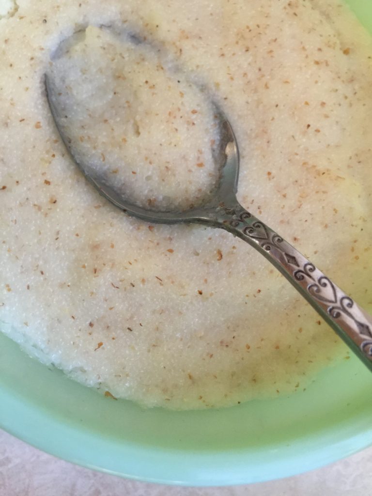 Another bowl of cream of wheat with a spoon, in a light green bowl, not as appetizing looking as the previous bowl.