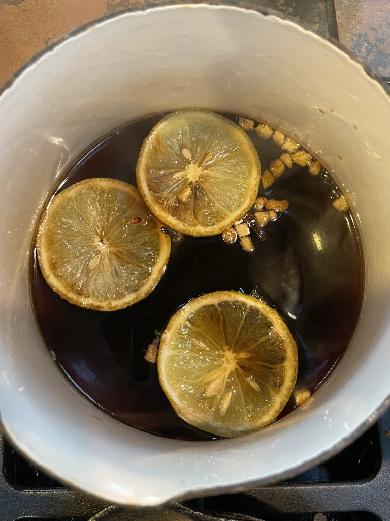 A pot of dark brown liquid with cloves and lemon slices in it.