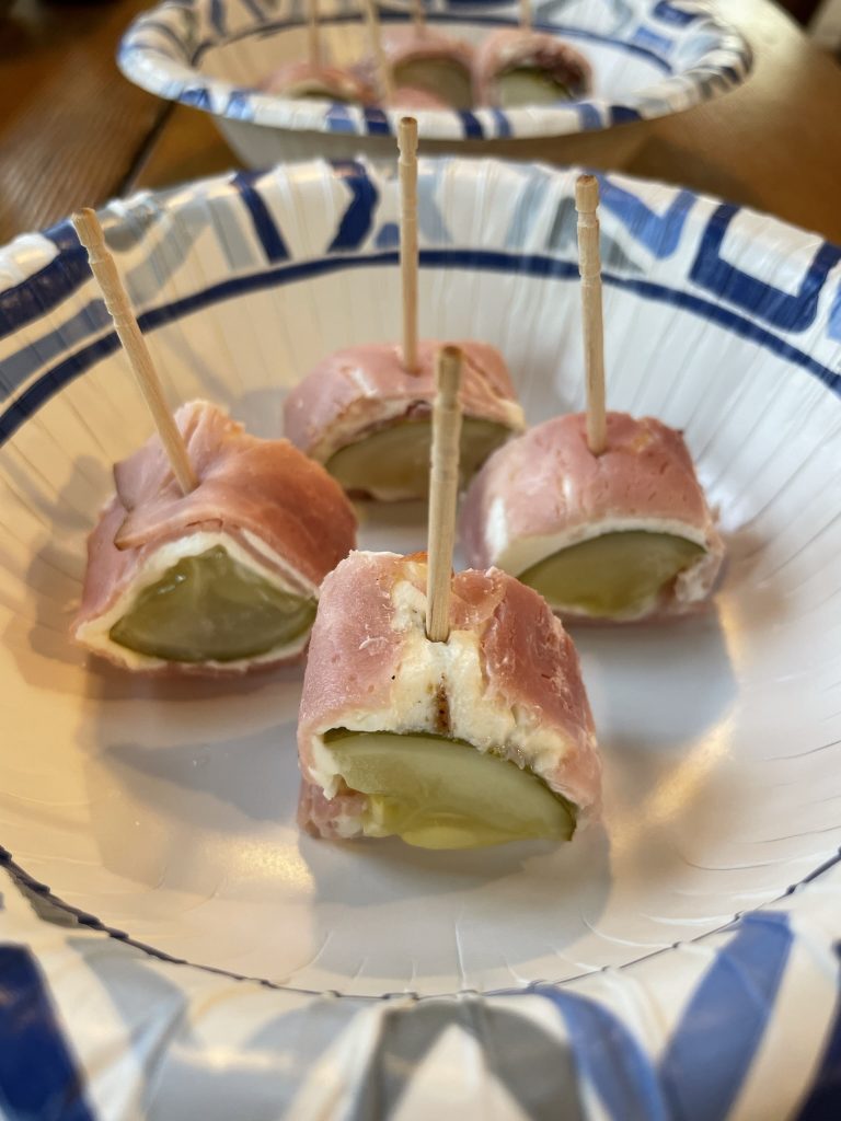 Pieces of cut pickle spears with cream cheese and ham around them. All four bites are cut like sushi rolls and held together with toothpicks. They are sitting atop a paper plate.