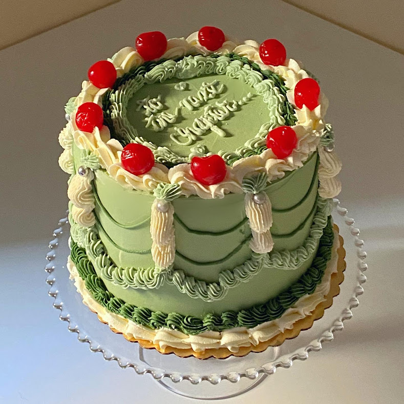 A layer cake decorated with green icing and maraschino cherries on it.