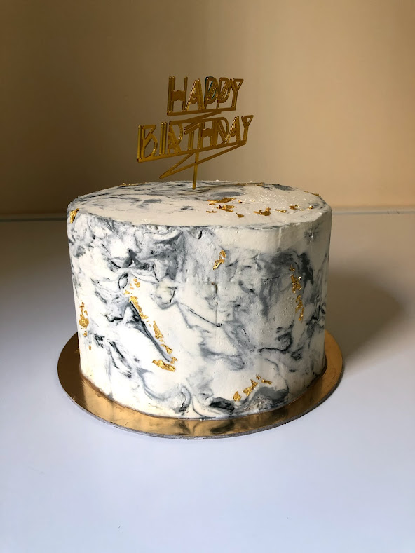A layer cake that is decorated with a white and gray marble design with gold flecks and a gold 
