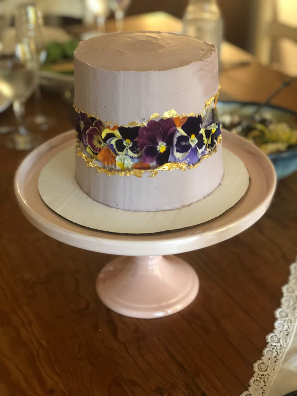 A layer cake that is decorated with lavender icing and edible flowers