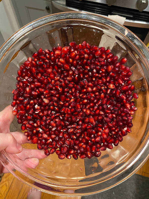 a hand holding a clear glass bowl full of pomegranate seeds