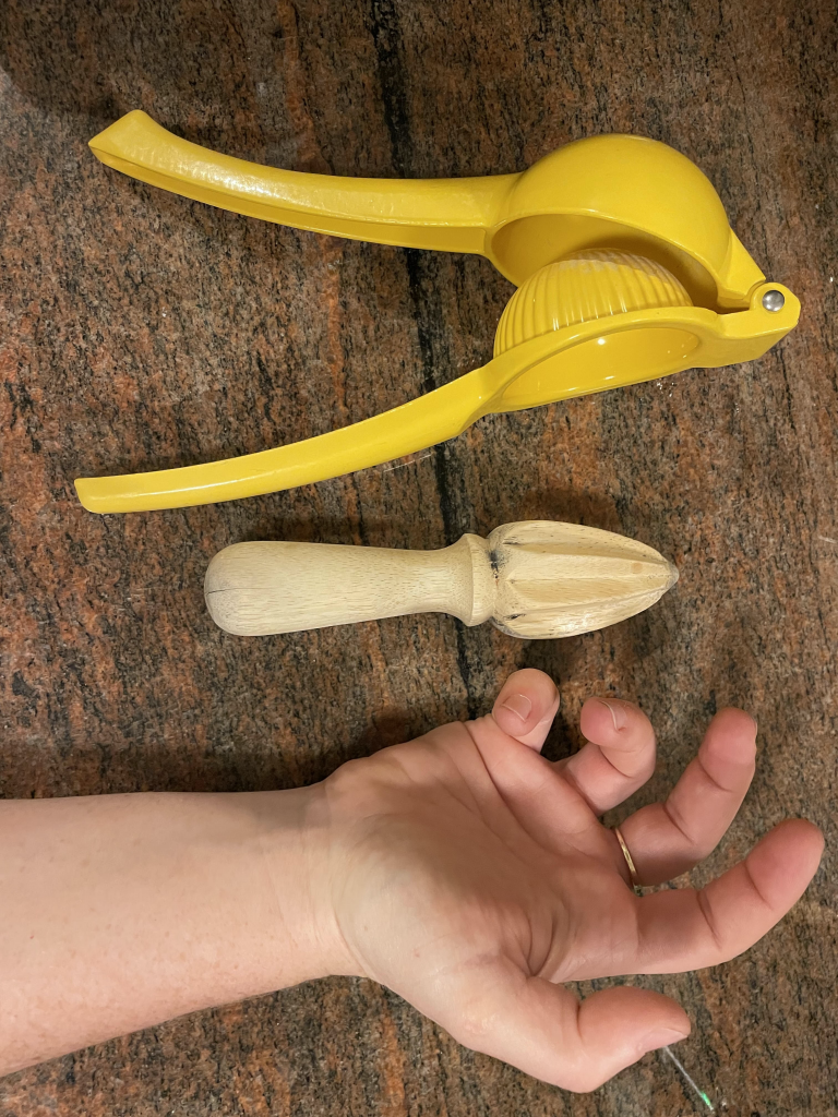 A yellow lever citrus squeezer, a wooden citrus reamer, and a person's hand