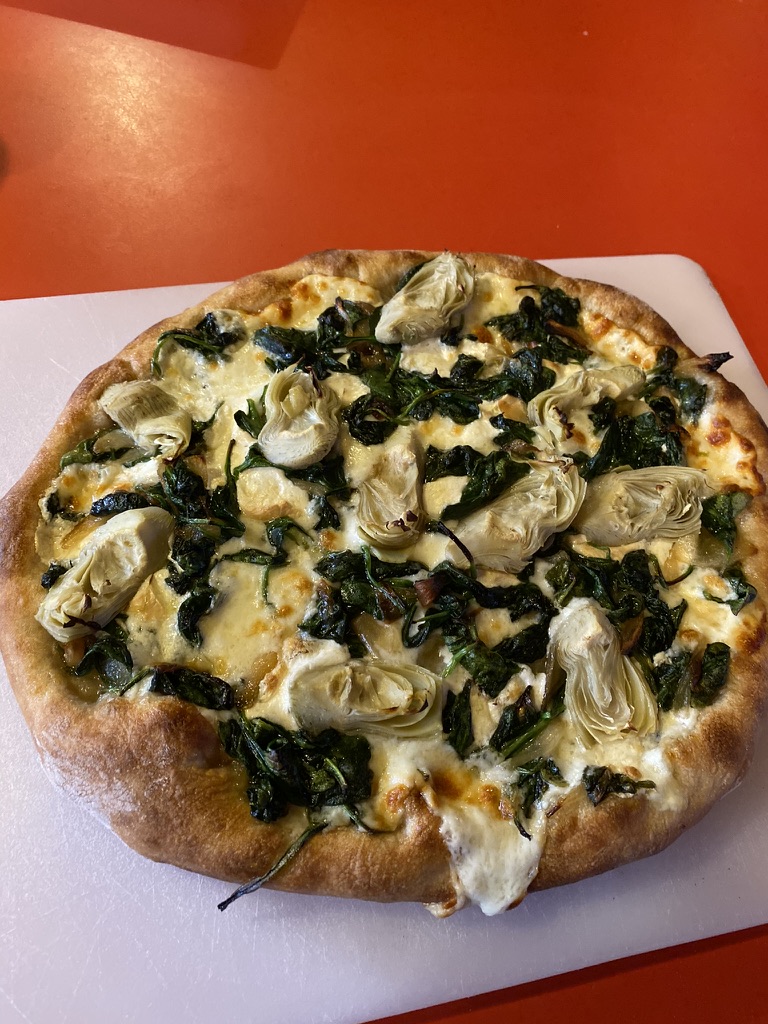 A homemade pizza with spinach, artichoke and oozing cheese
