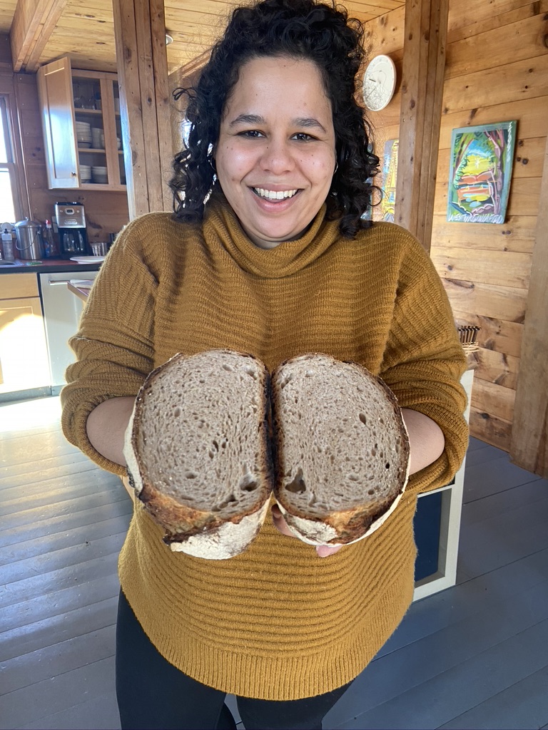 A happy woman holding two halves of a sourdough loaf