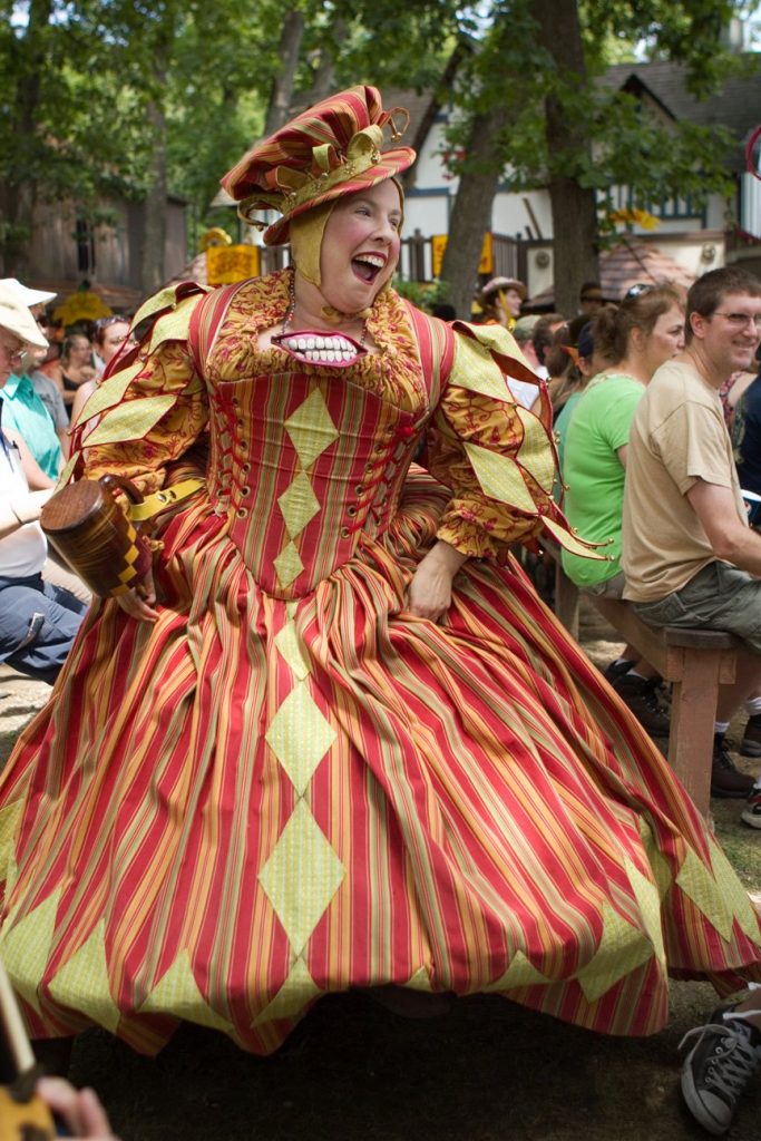 A dancing woman in a red, orange and lime green Renaissance Court Jester costume