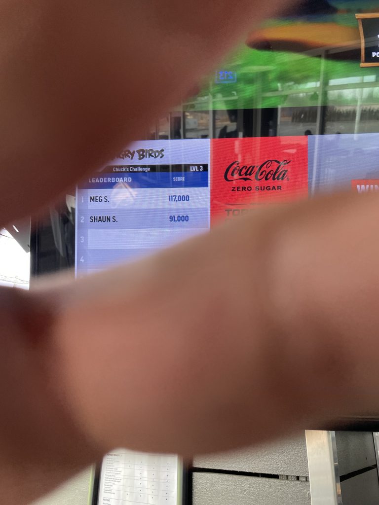A hand covering the camera lens, as a photo is taken of a Top Golf score board