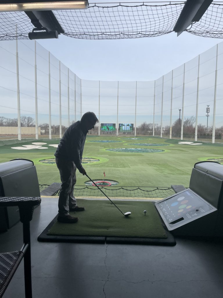 A man getting ready to swing a golf club at Top Golf, which looks like a miniature fenced in driving range