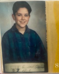 Abe Forman as a teenager in his yearbook photo. He's wearing a plaid blue and green collard long-sleeve shirt