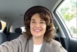 Diane Franklin wearing a hat, and grey coat. She's sitting in her car and has great hair.