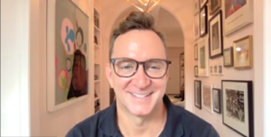 Clinton Kelly smiling at us from his Zoom window. His in his hallway wearing glasses.