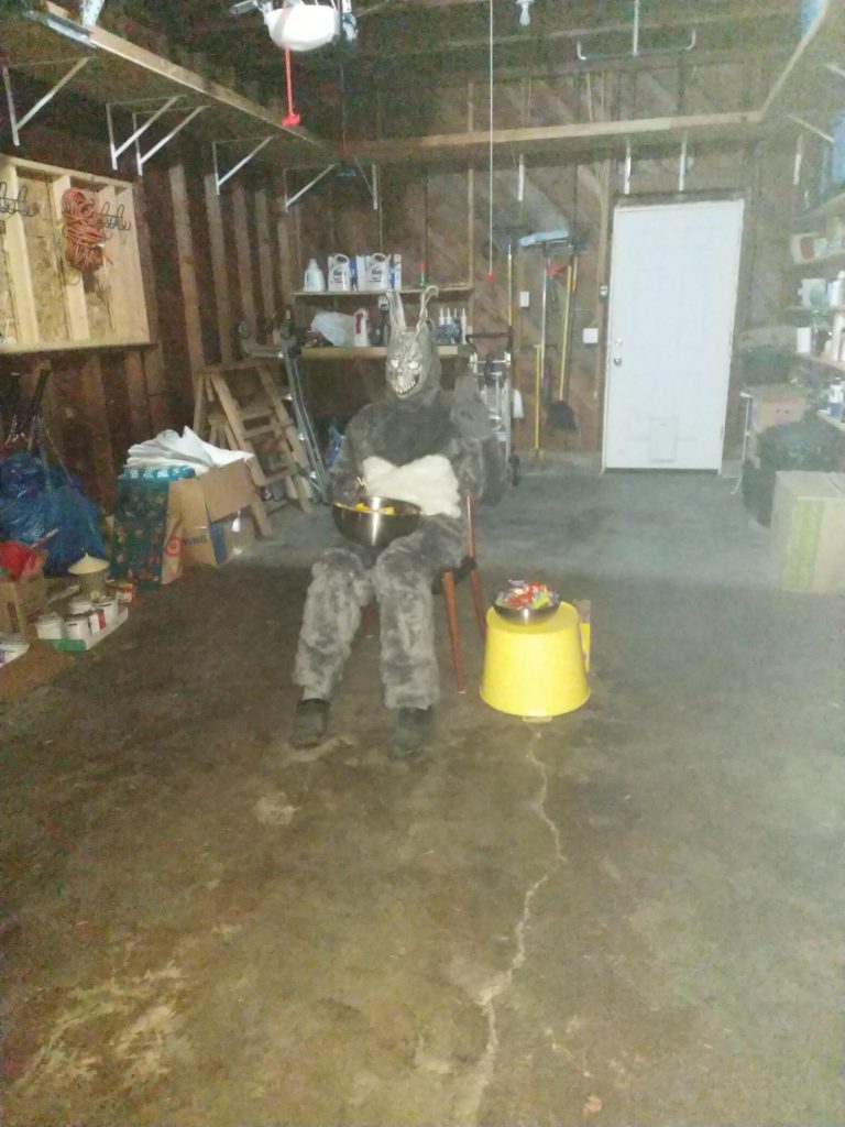 A man in a garage wearing a creepy bunny costume holding a bowl of candy