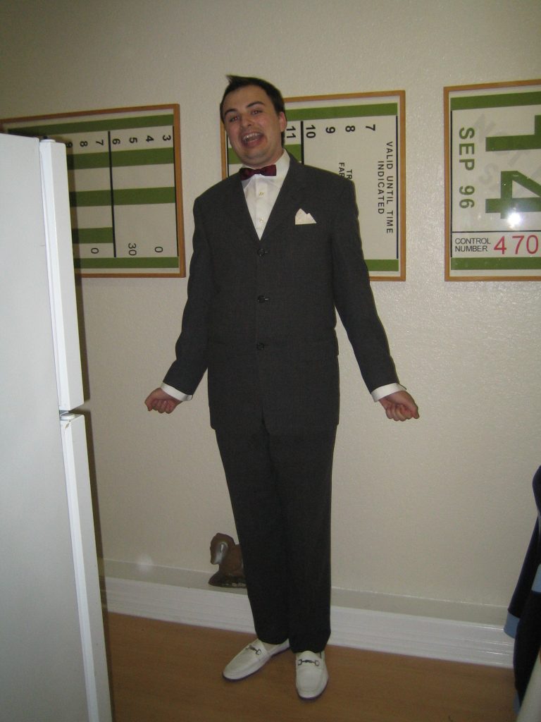 A man dressed in a gray suit, red bow tie, and white shoes