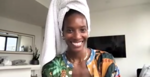 Zainab Johnson in a zoom window smiling at the camera. She's wearing a towel on her head!