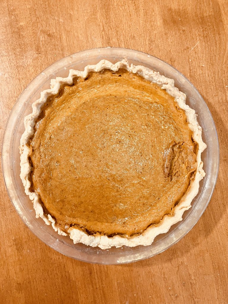 A pumpkin pie with a few imperfections on a wooden countertop