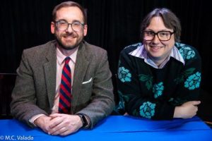 Brad Rtter wearing a suit with a red and blue striped tie. Wiley Wiggins is wearing a floral sweater with a collared shirt.