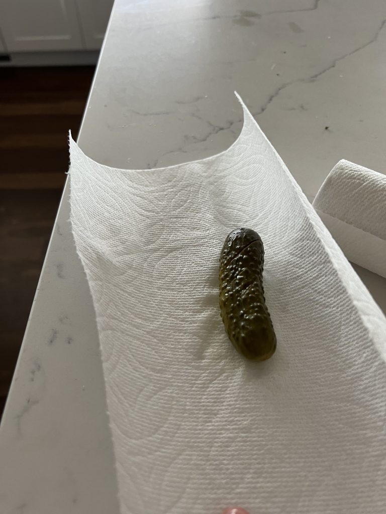 A photo of a pickle on a paper towel, sitting on a white marble countertop.