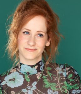 Christine Weatherup today! She's wearing a floral print shirt and is in front of a green background. Her hair is tastefully messy and her eyes match the green of the background.