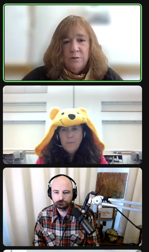 A screenshot of three Zoom windows, arranged vertically. At top is a woman in her 50s with shoulder-length blonde hair, against a blurred background. In the middle is another woman in her 50s with black hair, wearing a yellow hood that looks like Winnie-the-Pooh's face. At bottom is Bailiff Jesse Thorn, a bald man with a moustache, wearing headphones and a flannel shirt and speaking into a microphone.