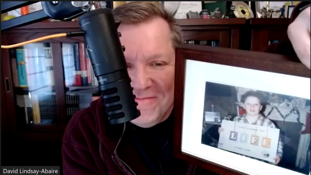 David Lindsay-Abaire holding up a framed photo of his brother, who is holding a box set of the board game Life
