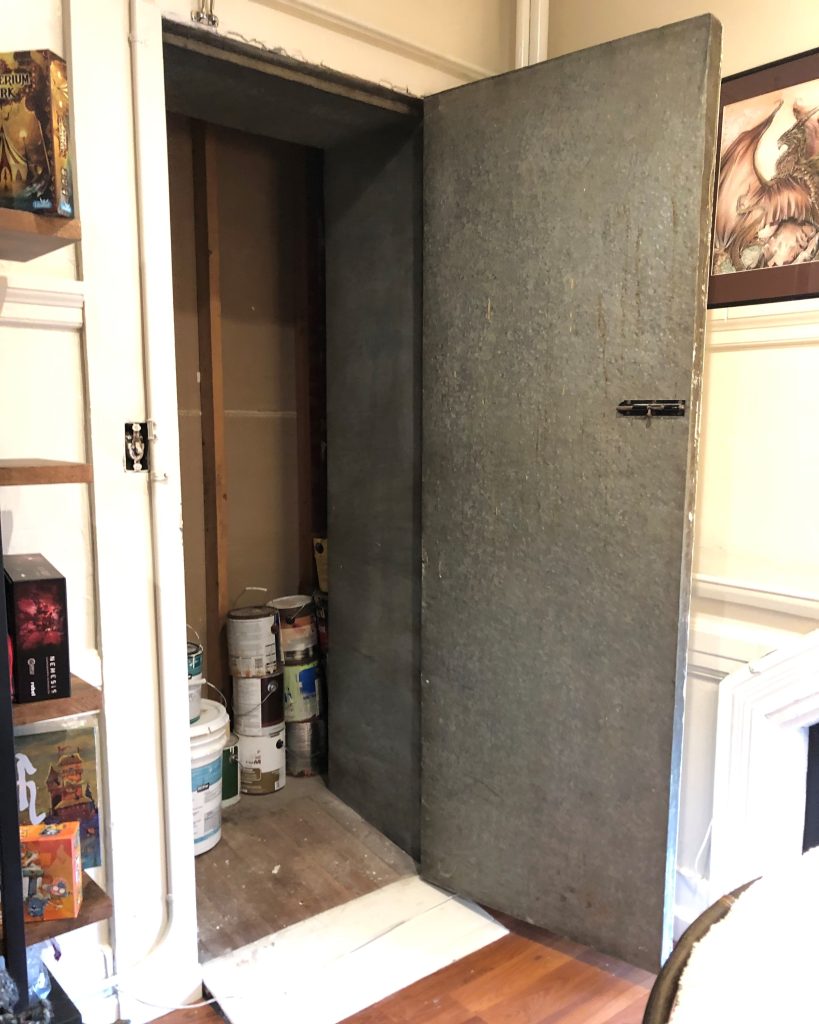 An opened door, leading to a small black closet. There are paint cans stacked in the corner of the closet.