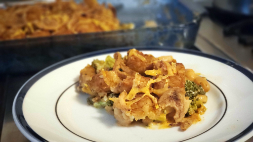 A serving of food on a white plate. Broccoli, cheddar cheese, tater tots, and fried onions are visible.