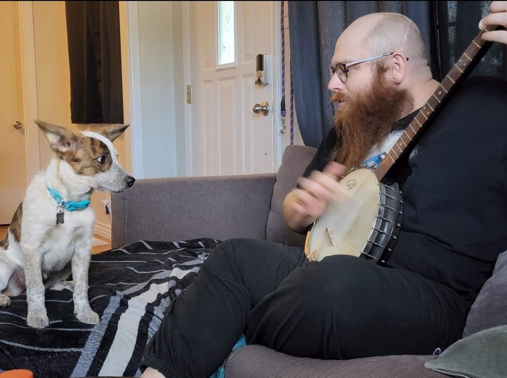 A man playing banjo for an interested dog