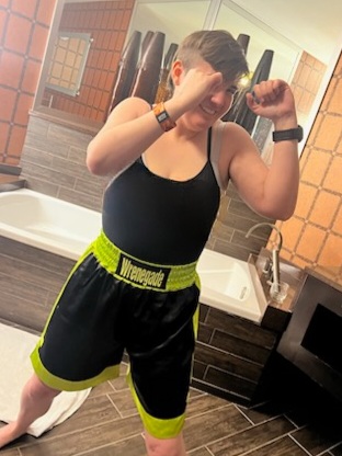A woman with fists up as if too get ready to fight, wearing silk boxing shorts