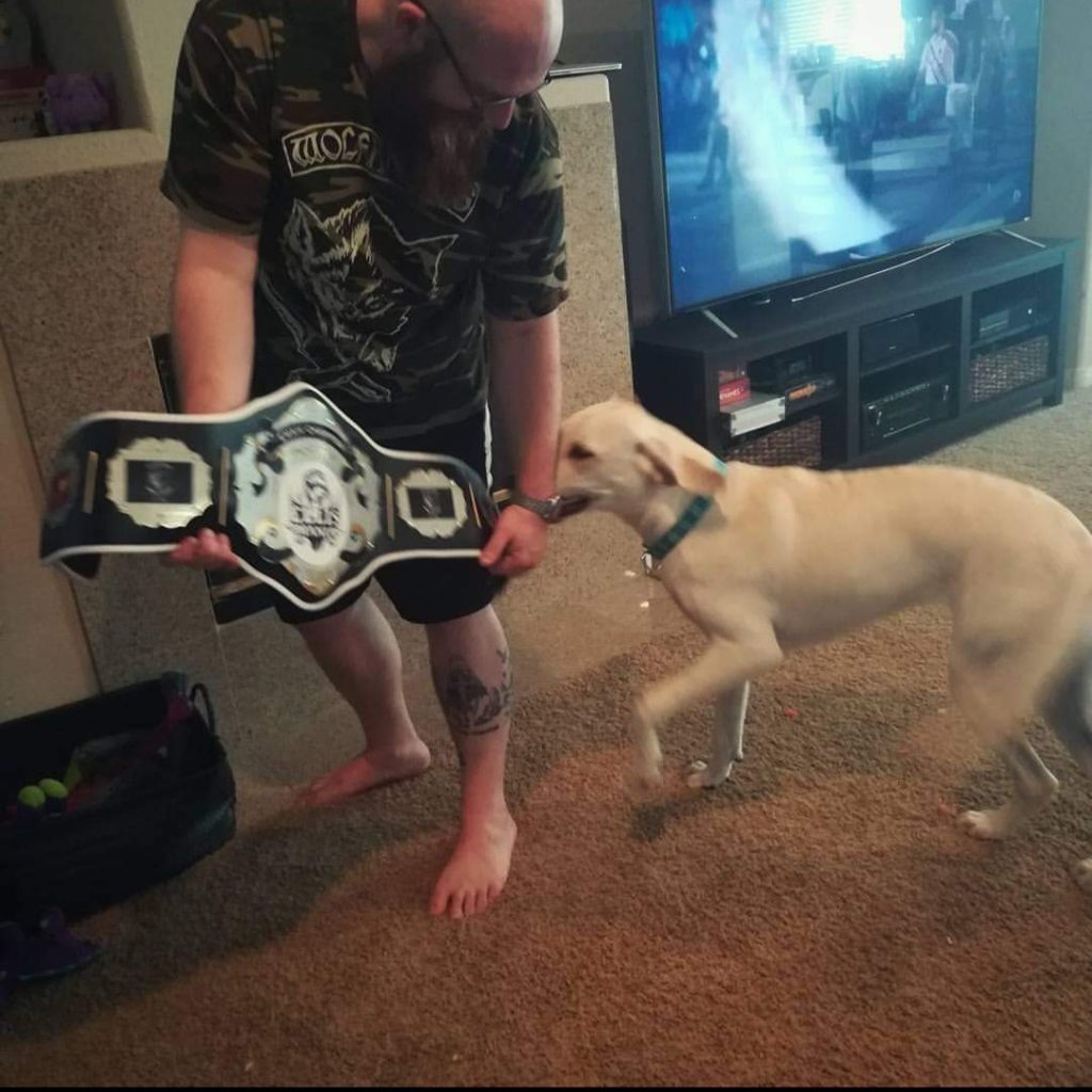 A man holding a boxing belt next to a dog