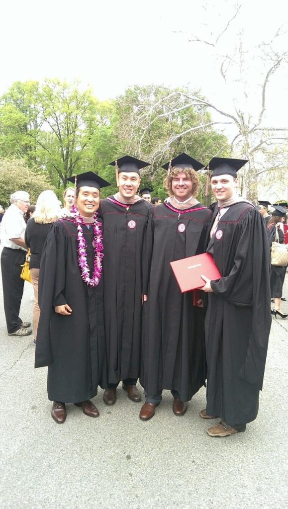 Four guys posed together wearing graduation caps and gowns