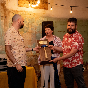 Worker-owners Kevin Ferguson and K.T. Wiegman presenting a plaque with a hammer on it to network founder Jesse Thorn