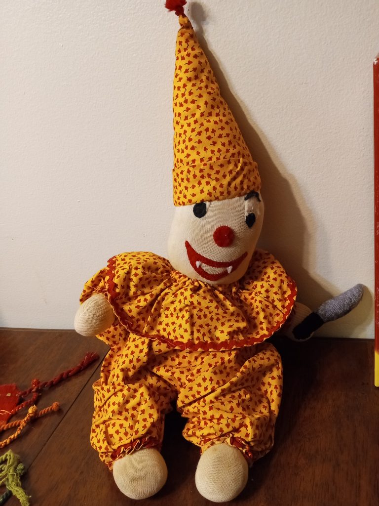 A stuffed toy clown with a yellow outfit, holding a little fabric knife
