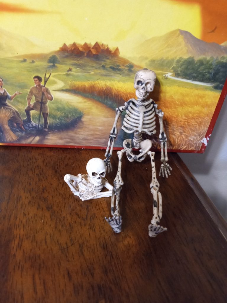 One toy skeleton that looks like it is crawling out of the table it's set on. Another skeleton sitting next to it.